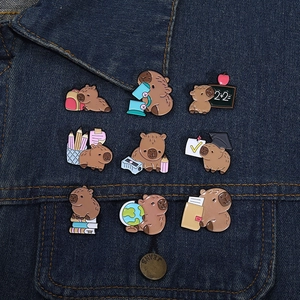 Detailed close-up of nine cute capybara enamel pins on blue denim fabric in school themes