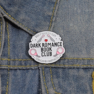Emaille-Anstecknadel Dark Romance Book Club mit rosa Handschellen auf einer Jeansjacke