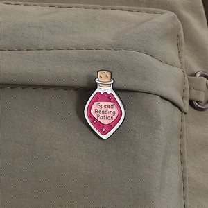 Close-up of Speed Reading Potion enamel pin on a green canvas backpack strap