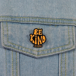 Close-up of a Be Kind Of A Bitch orange enamel pin on a denim jacket pocket