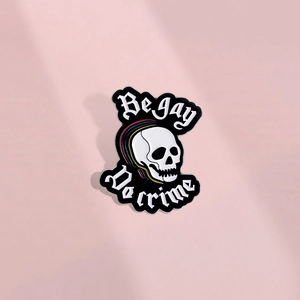 Détail du pin's en émail Be Gay Do Crime avec un crâne blanc et motifs arc-en-ciel