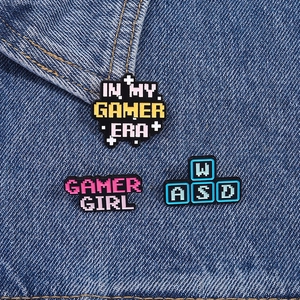 Close-up of three pixel-art gamer girl pins attached to blue denim jacket fabric