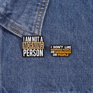 Close-up of enamel phrase brooches pinned on denim jacket showing metal texture
