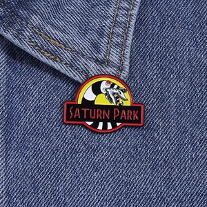 Close-up of Sandworm Saturn Park enamel pin on a blue denim jacket collar with vivid colors
