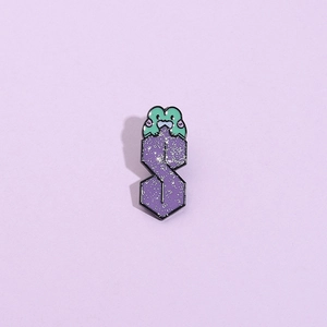 Spilla smaltata a forma di S viola con ranocchia verde e glitter argento su sfondo lilla