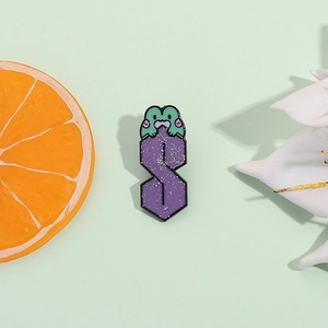 Spilla smaltata con lettera S viola glitterata e rana verde su sfondo pastello