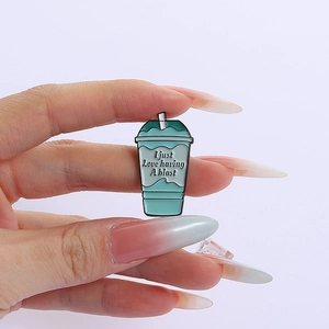 Close-up of a mint green enamel beverage cup pin with straw and motivational text