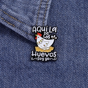 Funny chicken enamel pin with Spanish text on blue denim jacket, cute animal brooch accessory