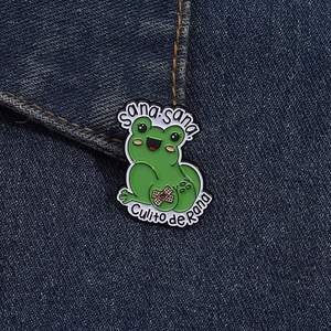 Makroaufnahme der grünen Emaille-Froschbrosche mit Sana sana Text auf Denimstoff
