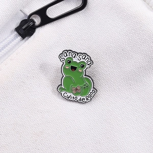 Detail der Zeichentrick Frosch Emaille-Anstecknadel mit Sana Sana Text auf weißem Stoff