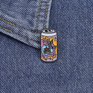 Macro shot of colorful juice can enamel pin with Yes You Can text on blue denim