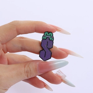 Dettaglio macro di una spilla smaltata viola a forma di S con un piccolo ranocchio