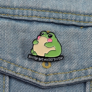 Cute green frog enamel pin with Rootin' But Mostly Tootin' text on a denim jacket