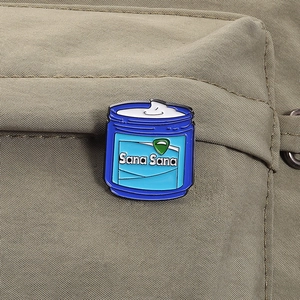 Creative blue bottle enamel brooch with Sana Sana lettering on a khaki fabric background