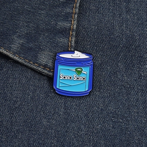 Close-up of a blue and white jar-shaped enamel pin on a blue denim jacket texture