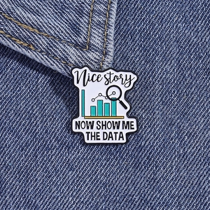 Macro detail of data analysis enamel brooch showing bar charts and magnifying glass on denim