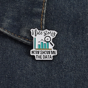 Macro detail of enamel brooch with data charts and 'NOW SHOW ME THE DATA' text on denim