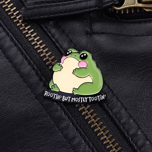 Detailed close-up of a green round frog enamel pin on a black leather jacket background