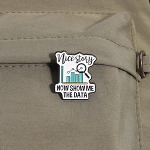 Macro shot of an enamel data chart brooch with 'Show me the data' text on canvas bag