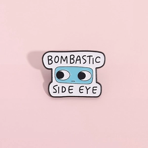 Spilla smaltata Bombastic Side Eye blu e bianca su sfondo rosa alla moda