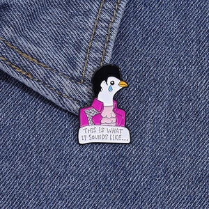 Detail of cartoon pigeon enamel pin with purple jacket pinned on blue denim fabric