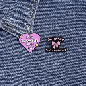 Pink heart and bow enamel pins with 'Literally Just a Girl' text on denim fabric