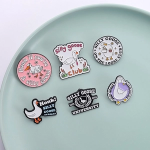 Assorted cute enamel goose pins with humorous phrases on a green ceramic display plate