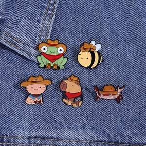Close-up of enamel cowboy animal pins including frog and capybara on denim fabric