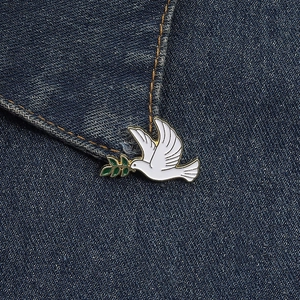 Macro shot of a white peace dove brooch with olive branch on blue denim fabric