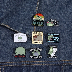 Set of funny green enamel frog pins shown on a denim jacket pocket as decorative badges