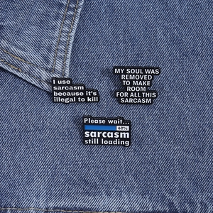 Detailansicht der schwarzen Emaille-Anstecknadeln mit Sprüchen auf Denim-Stoff