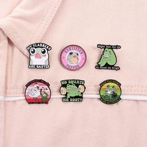 Set of 6 humorous green frog enamel pins displayed on pink denim fabric texture