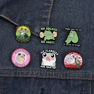 Close-up of funny frog enamel pins on denim fabric showing various humorous designs