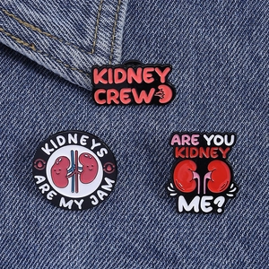 Detailed view of three enamel kidney pins with medical puns on blue denim fabric