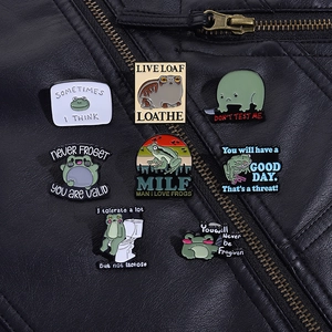 Detail view of funny green enamel frog pins with humorous text on a black leather jacket