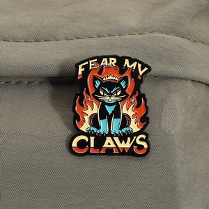 Detail der kreativen schwarzen Emaille-Anstecknadel mit Flammen und Fear My Claws Spruch