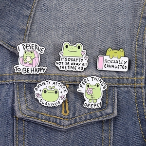 Five cute green frog enamel pins with text on a denim jacket for clothes accessories
