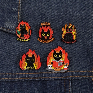 Detail of five black cat enamel pins featuring arson and funny slogans on blue denim fabric