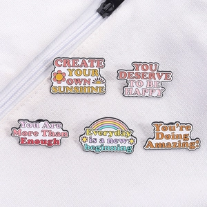 Dettaglio di cinque spille in smalto colorate con citazioni motivazionali su maglia