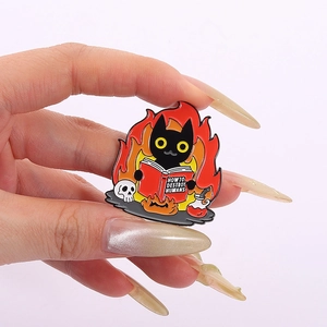Macro shot of a black cat enamel pin reading a book named How to Destroy Humans