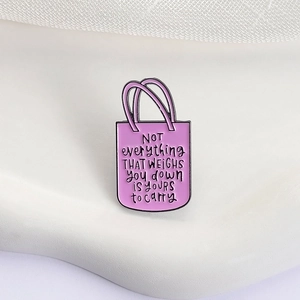 Détail d'une broche sac en émail lavande avec bordure noire et texte manuscrit