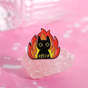Macro view of black cat enamel pin with flames and Arson text on pink crystal background