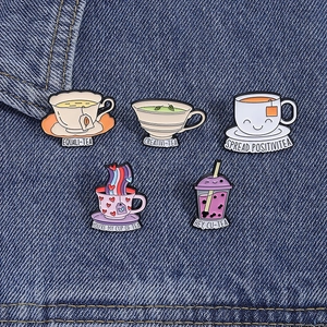 Close-up of five enamel tea cup pins featuring funny puns on blue denim fabric