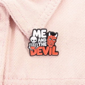 Close-up of enamel skull and red devil pin on pink denim with Me and the Devil text