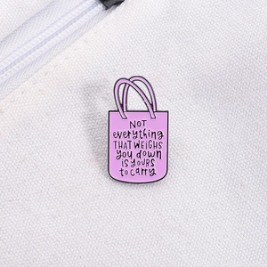 Gros plan détaillé d'un pin's en émail violet en forme de sac avec texte sur toile blanche