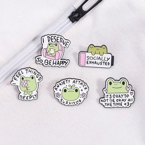Set of 5 cute green frog enamel pins with mental health phrases on white canvas fabric