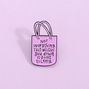 Détail d'un pin's émaillé rose en forme de sac avec texte de motivation sur fond violet