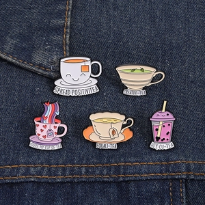Close-up of colorful enamel tea cup brooches with puns on premium blue denim fabric