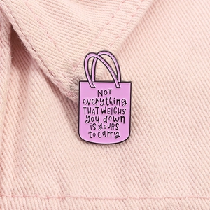 Gros plan d'une broche en émail rose en forme de sac avec citation inspirante