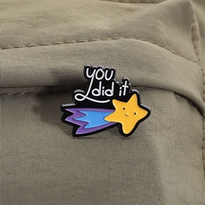 Detail of cute meteor enamel pin with you did it text on olive green fabric background